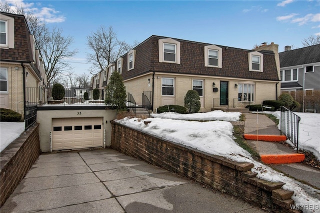 front facade featuring concrete driveway, mansard roof, roof with shingles, and brick siding