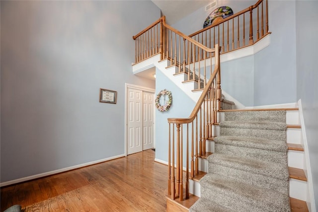 staircase featuring a high ceiling, wood finished floors, visible vents, and baseboards