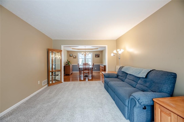 carpeted living area featuring a notable chandelier, visible vents, and baseboards