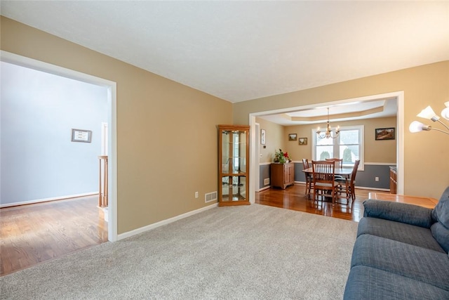 living area with visible vents, baseboards, carpet, a tray ceiling, and a chandelier