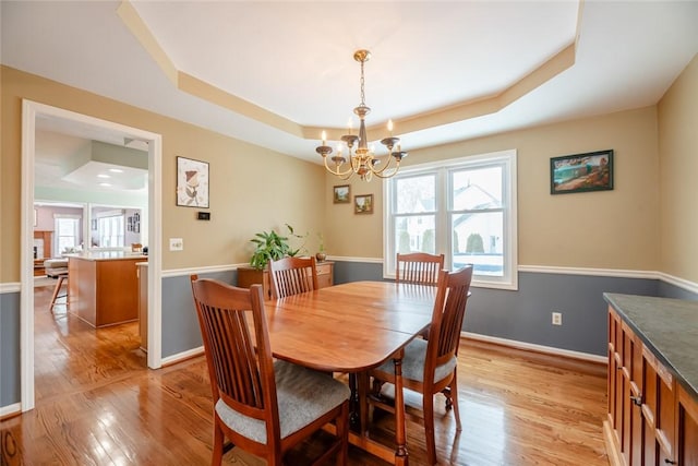 dining space featuring a chandelier, light wood-type flooring, a raised ceiling, and baseboards