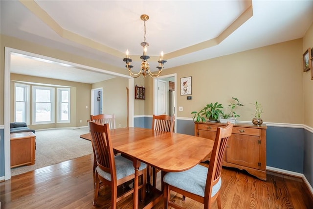 dining space featuring a chandelier, light wood finished floors, a raised ceiling, and baseboards