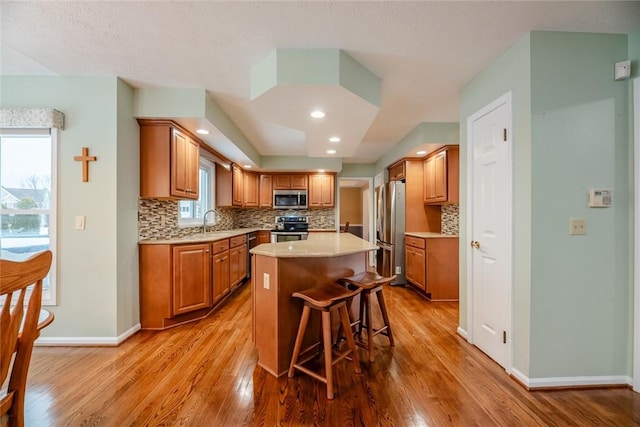 kitchen featuring a center island, light countertops, appliances with stainless steel finishes, light wood-style floors, and a sink