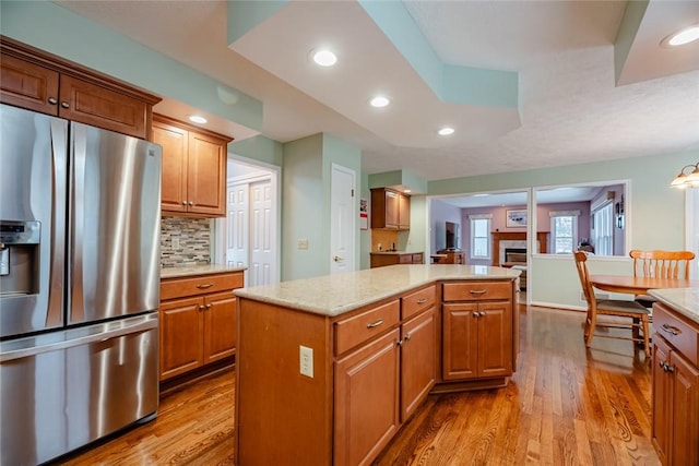 kitchen with wood finished floors, stainless steel refrigerator with ice dispenser, a kitchen island, and brown cabinets