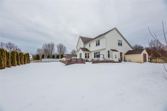 snow covered rear of property with a shed, fence, and an outdoor structure