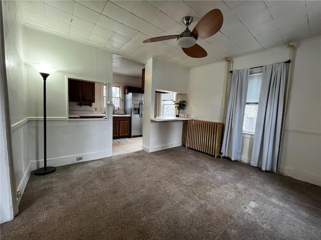 unfurnished living room featuring baseboards, a ceiling fan, radiator, ornamental molding, and carpet