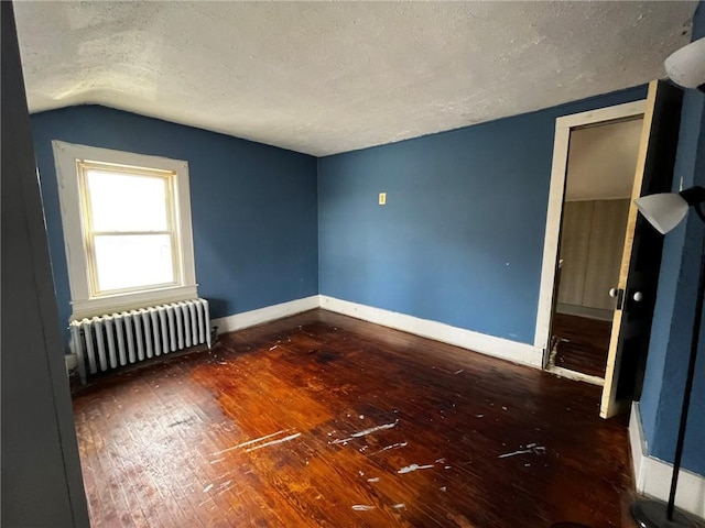 spare room featuring baseboards, radiator, lofted ceiling, wood-type flooring, and a textured ceiling