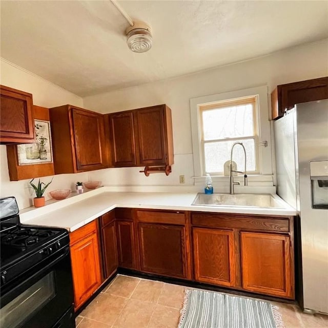 kitchen with a sink, light countertops, black range with gas stovetop, brown cabinetry, and stainless steel fridge