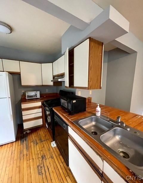 kitchen with black appliances, under cabinet range hood, white cabinets, and a sink