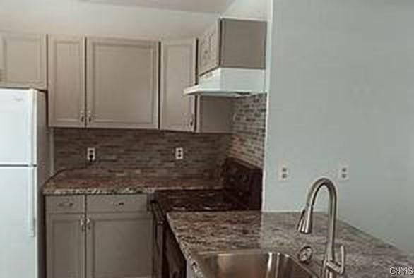 kitchen featuring stone countertops, tasteful backsplash, custom range hood, freestanding refrigerator, and a sink