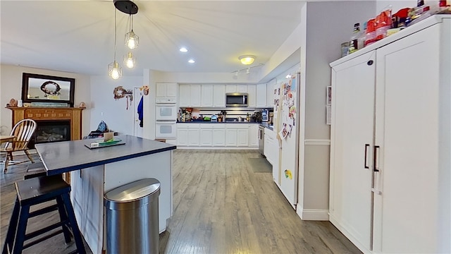 kitchen featuring a fireplace, light wood finished floors, white cabinets, white appliances, and a kitchen breakfast bar