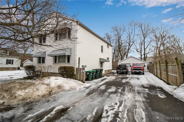 snow covered property featuring an outdoor structure, a detached garage, and fence