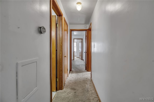 hallway featuring light carpet and baseboards