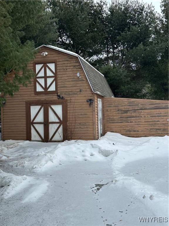 snow covered structure with a barn, a garage, fence, and an outdoor structure