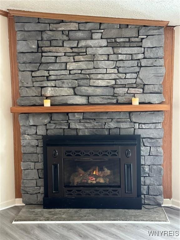 interior details featuring a textured ceiling, a fireplace, wood finished floors, and baseboards