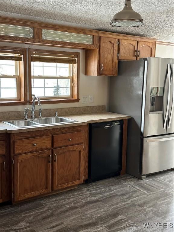 kitchen featuring brown cabinetry, dishwasher, light countertops, stainless steel refrigerator with ice dispenser, and a sink