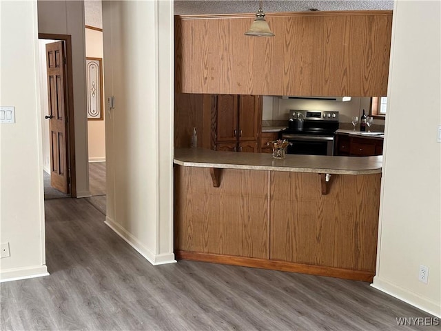 kitchen with a peninsula, a kitchen bar, wood finished floors, and stainless steel range with electric cooktop