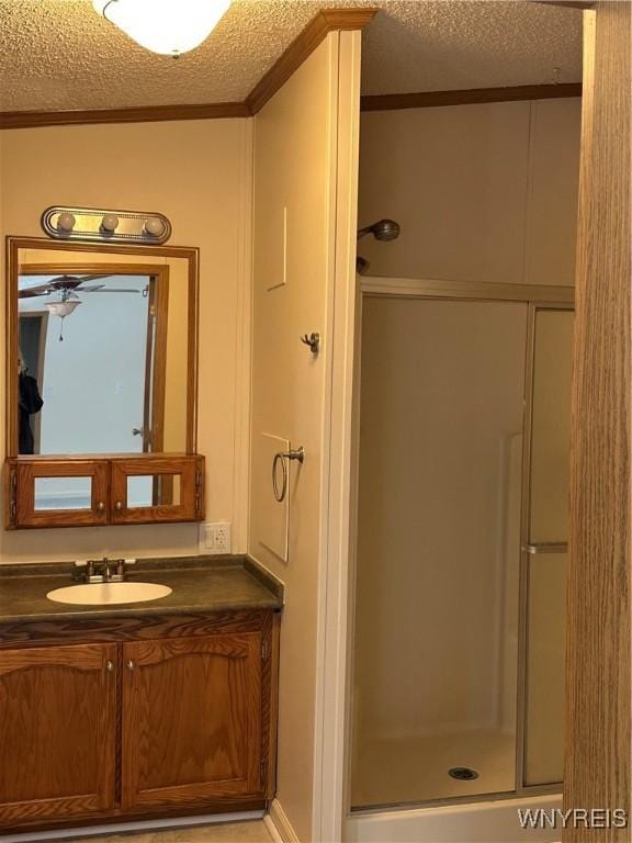 full bathroom featuring crown molding, a shower stall, a textured ceiling, and vanity