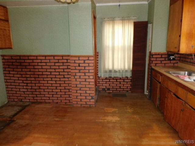 kitchen featuring brown cabinetry, light wood-style floors, a sink, and brick wall