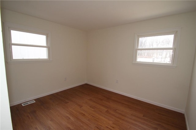 spare room featuring baseboards, wood finished floors, visible vents, and a healthy amount of sunlight