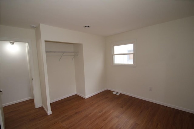 unfurnished bedroom featuring a closet, wood finished floors, visible vents, and baseboards