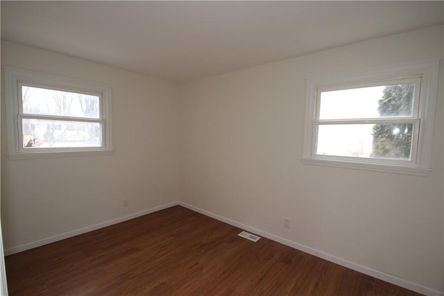 unfurnished room featuring a healthy amount of sunlight, visible vents, and dark wood-style flooring