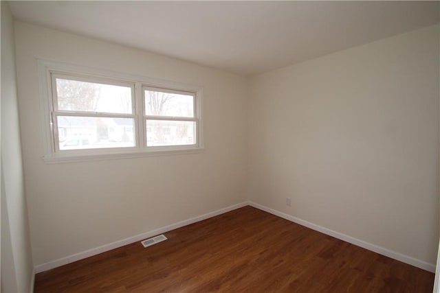 spare room featuring dark wood-style floors, visible vents, and baseboards