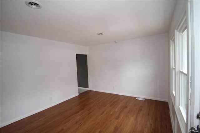 spare room with wood finished floors, visible vents, and baseboards