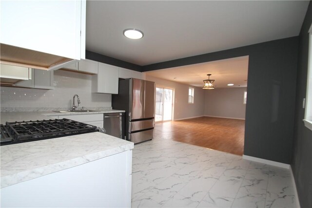 kitchen with a sink, marble finish floor, appliances with stainless steel finishes, light countertops, and decorative backsplash