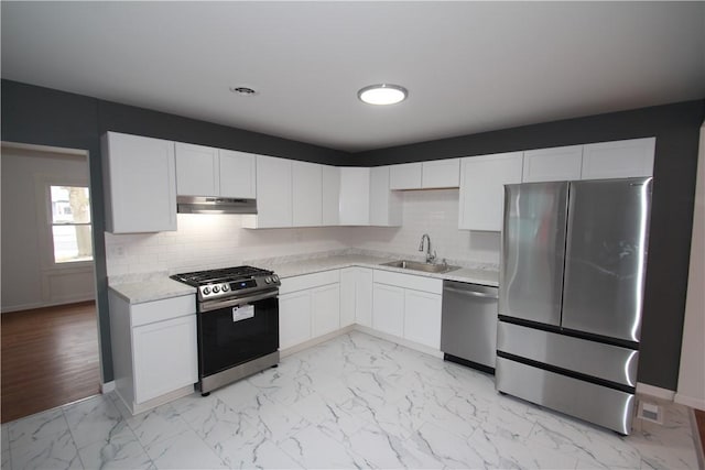 kitchen featuring decorative backsplash, marble finish floor, stainless steel appliances, under cabinet range hood, and a sink