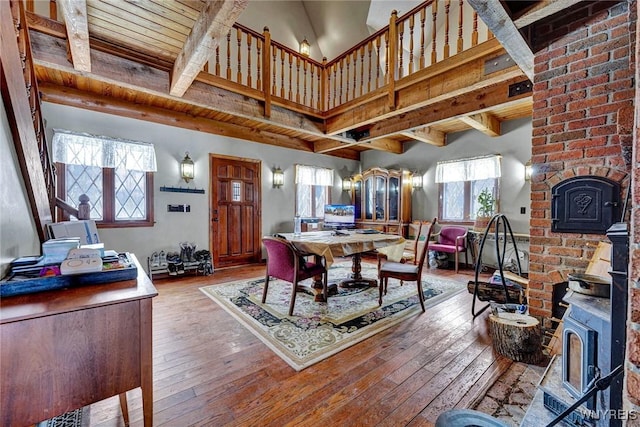 dining room with plenty of natural light, a wood stove, beamed ceiling, and hardwood / wood-style flooring