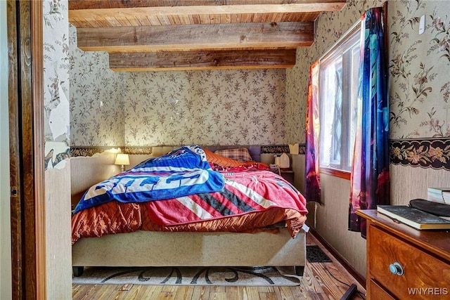 bedroom with wood finished floors, baseboards, beam ceiling, and wallpapered walls