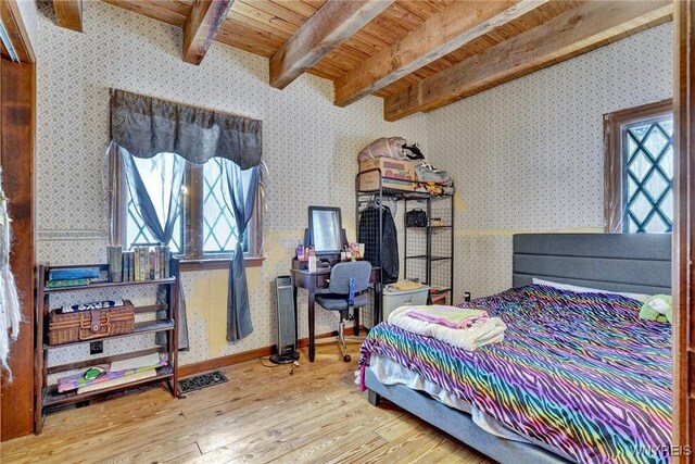 bedroom with wallpapered walls, wood-type flooring, multiple windows, and beam ceiling