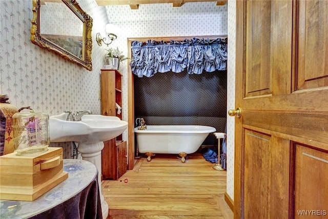 bathroom with wood finished floors, a freestanding bath, and wallpapered walls