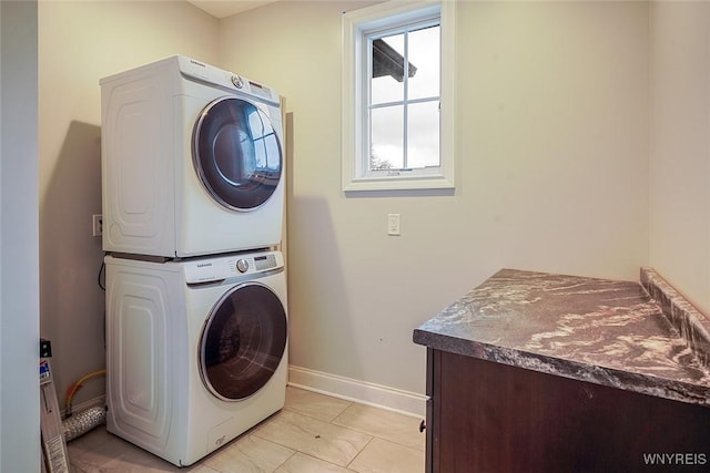 clothes washing area with light tile patterned floors, baseboards, cabinet space, and stacked washing maching and dryer