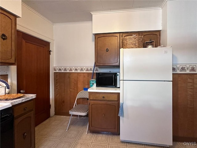 kitchen featuring a wainscoted wall, light countertops, ornamental molding, freestanding refrigerator, and wood walls