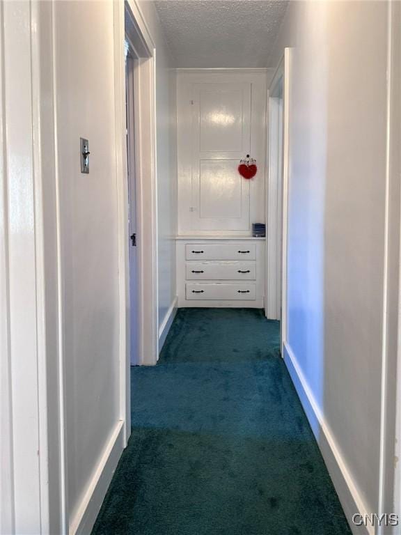 corridor with baseboards, dark colored carpet, and a textured ceiling