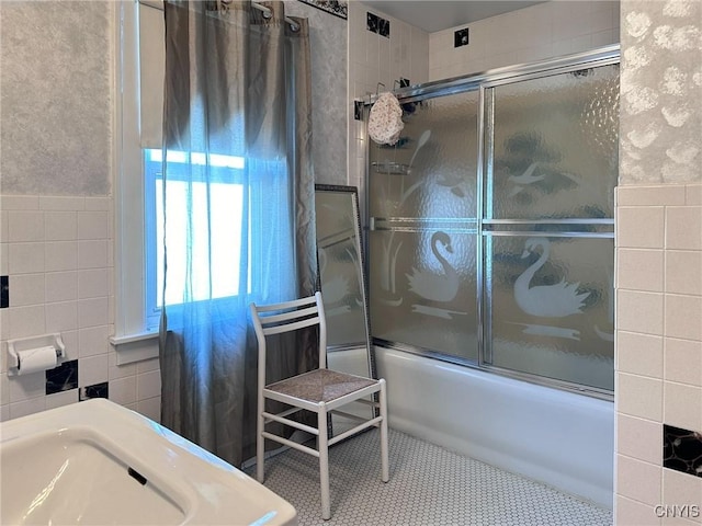 bathroom featuring tile patterned flooring, a sink, tile walls, and bath / shower combo with glass door