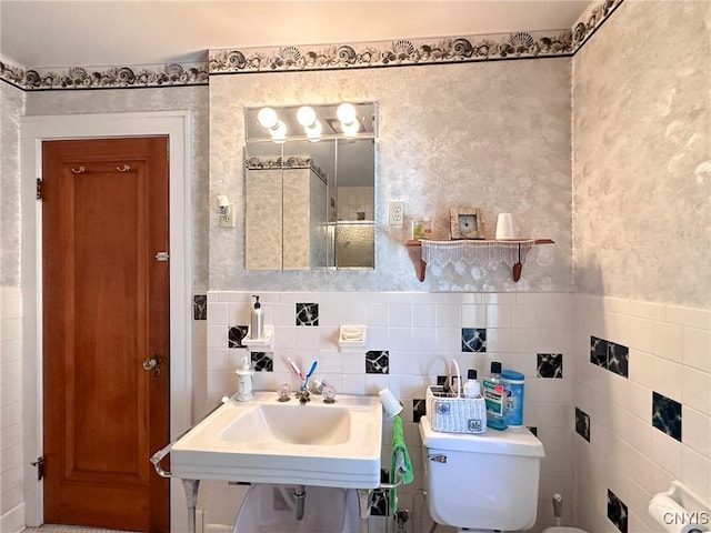 bathroom featuring a wainscoted wall, tile walls, toilet, a sink, and wallpapered walls