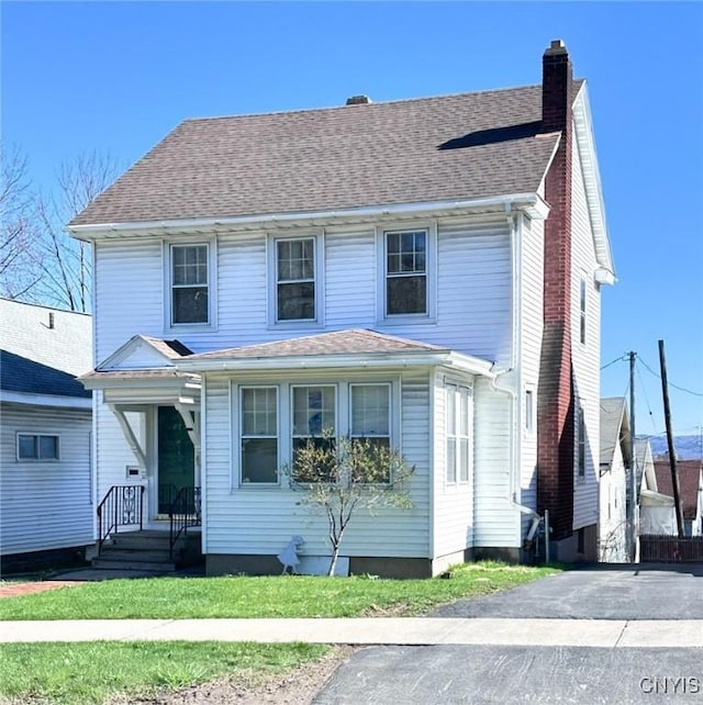 view of front of property with a front yard, a chimney, and roof with shingles