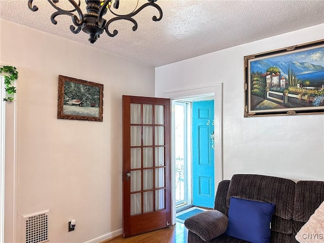 sitting room with visible vents, a textured ceiling, baseboards, and wood finished floors