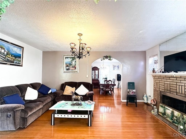 living area featuring arched walkways, a brick fireplace, a textured ceiling, wood finished floors, and a chandelier