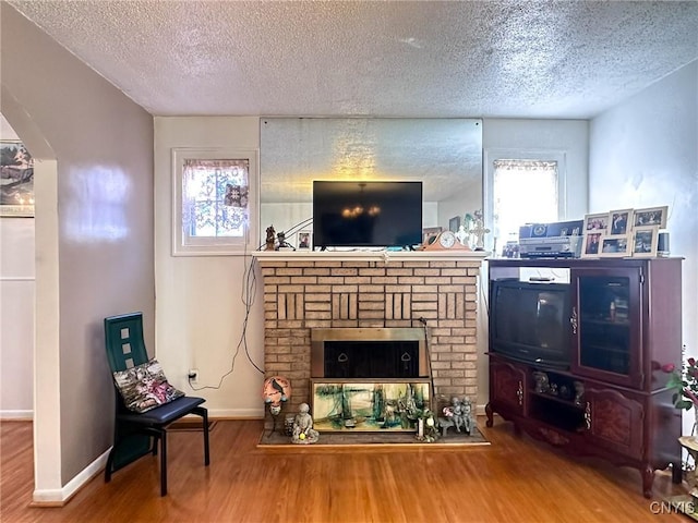 living area with arched walkways, a brick fireplace, wood finished floors, and baseboards