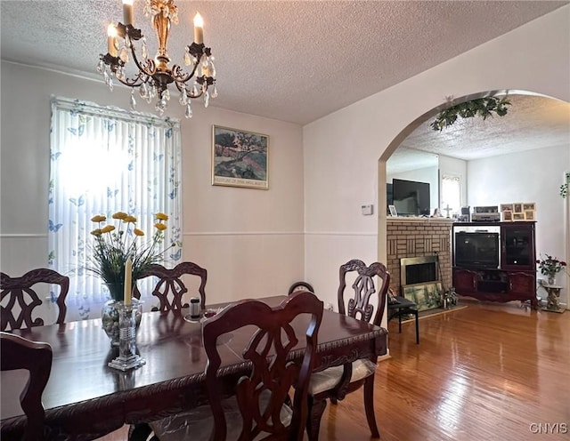 dining area with a textured ceiling, arched walkways, a brick fireplace, and wood finished floors