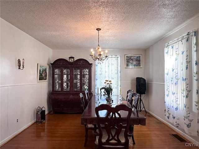 dining space with a notable chandelier, visible vents, a textured ceiling, wood finished floors, and baseboards