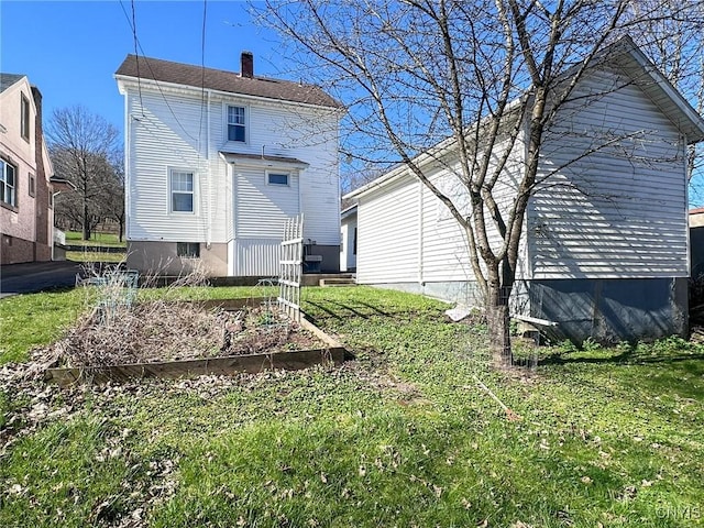 back of house featuring a lawn, a chimney, and a garden