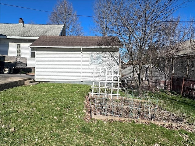 view of property exterior with a yard, a shingled roof, fence, and a garden