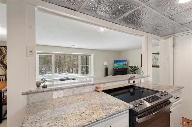 kitchen with stainless steel range with electric stovetop, an ornate ceiling, white cabinetry, and light stone counters