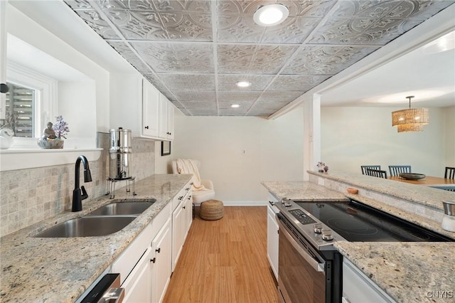 kitchen featuring tasteful backsplash, white cabinets, light wood-type flooring, a sink, and range with electric stovetop