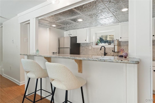 kitchen featuring decorative backsplash, an ornate ceiling, a kitchen breakfast bar, freestanding refrigerator, and white cabinetry